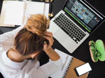O femeie care se confruntă cu anxietate și stă în fața laptopului cu mâinile în cap
